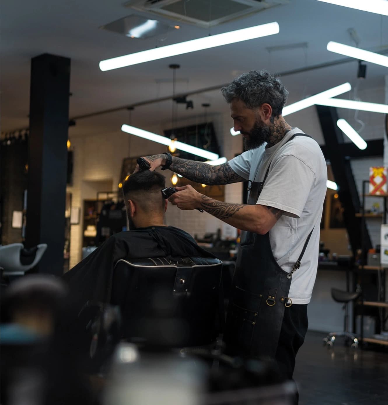 Barbier réalisant une coupe dégradée au clipper dans un barbershop